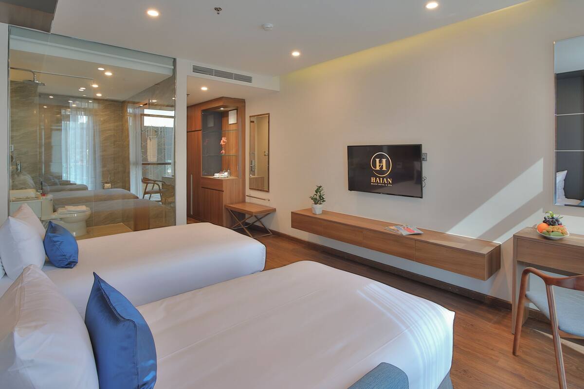 A modern hotel room with two beds, a desk, a TV, and a large mirror.