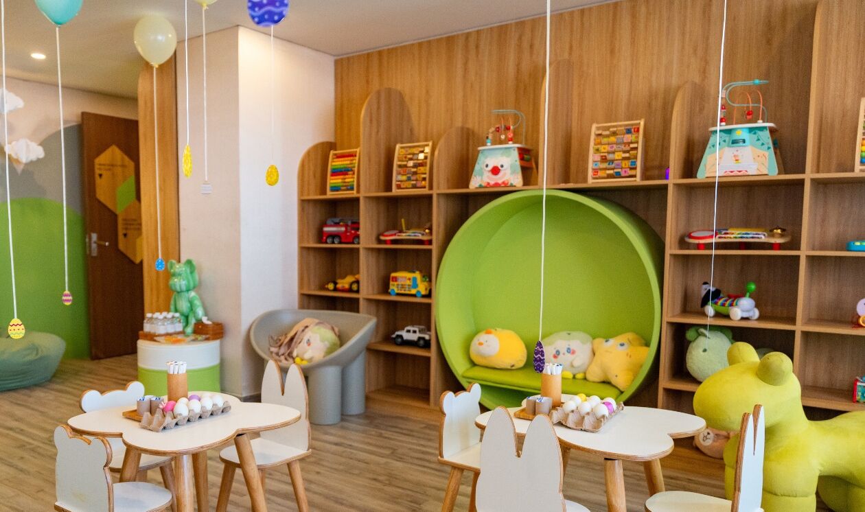 Un cuarto de juegos para niños con estantes de madera, una zona de juego verde y diversos juguetes y material educativo.