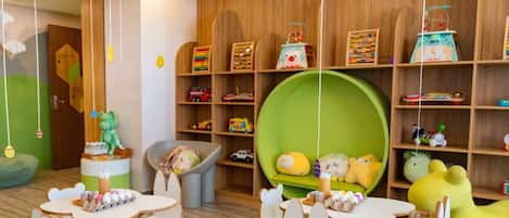 Un cuarto de juegos para niños con estantes de madera, una zona de juego verde y diversos juguetes y material educativo.