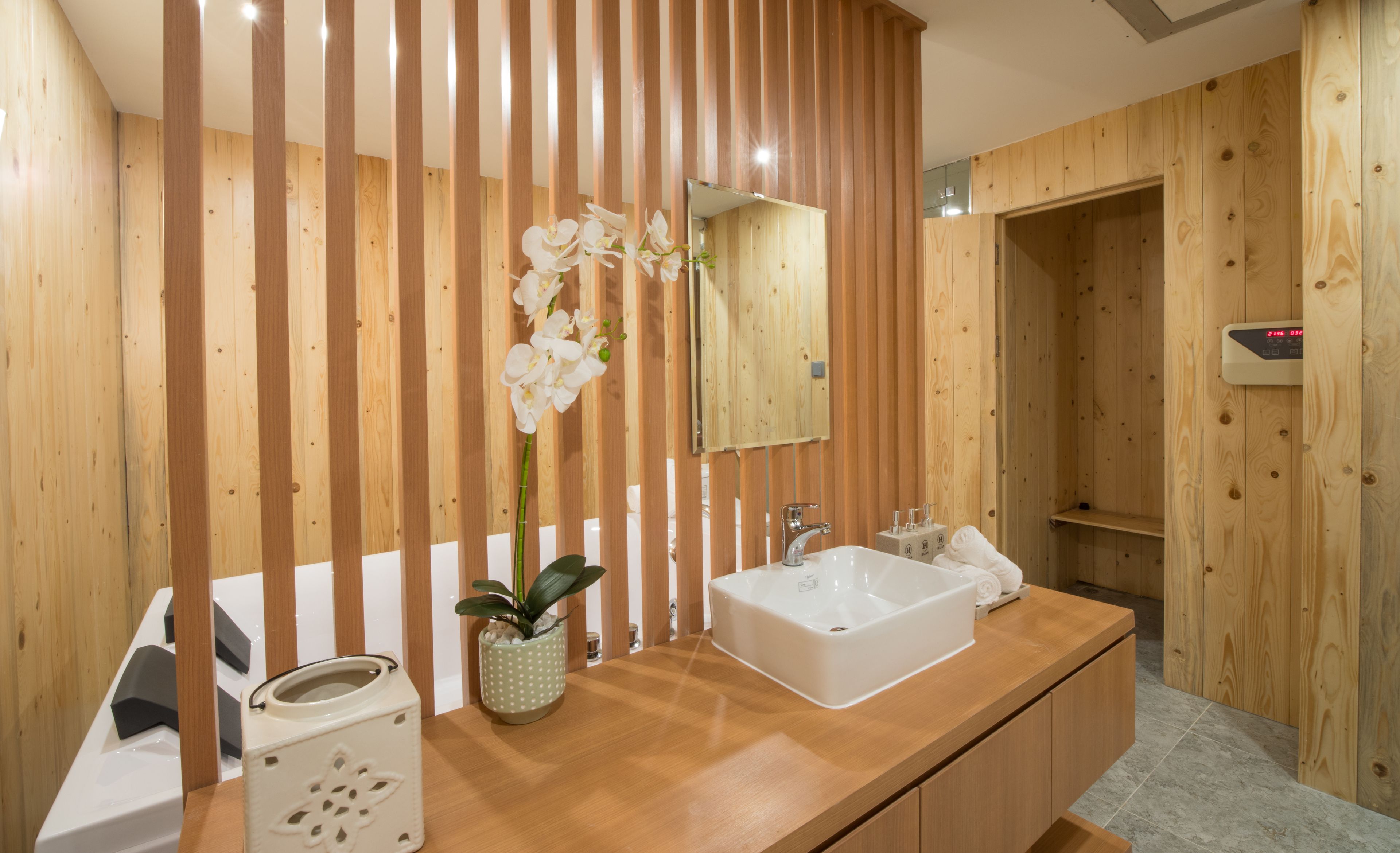 A modern bathroom with a wooden vanity, a large mirror, a white sink, and a shower area.