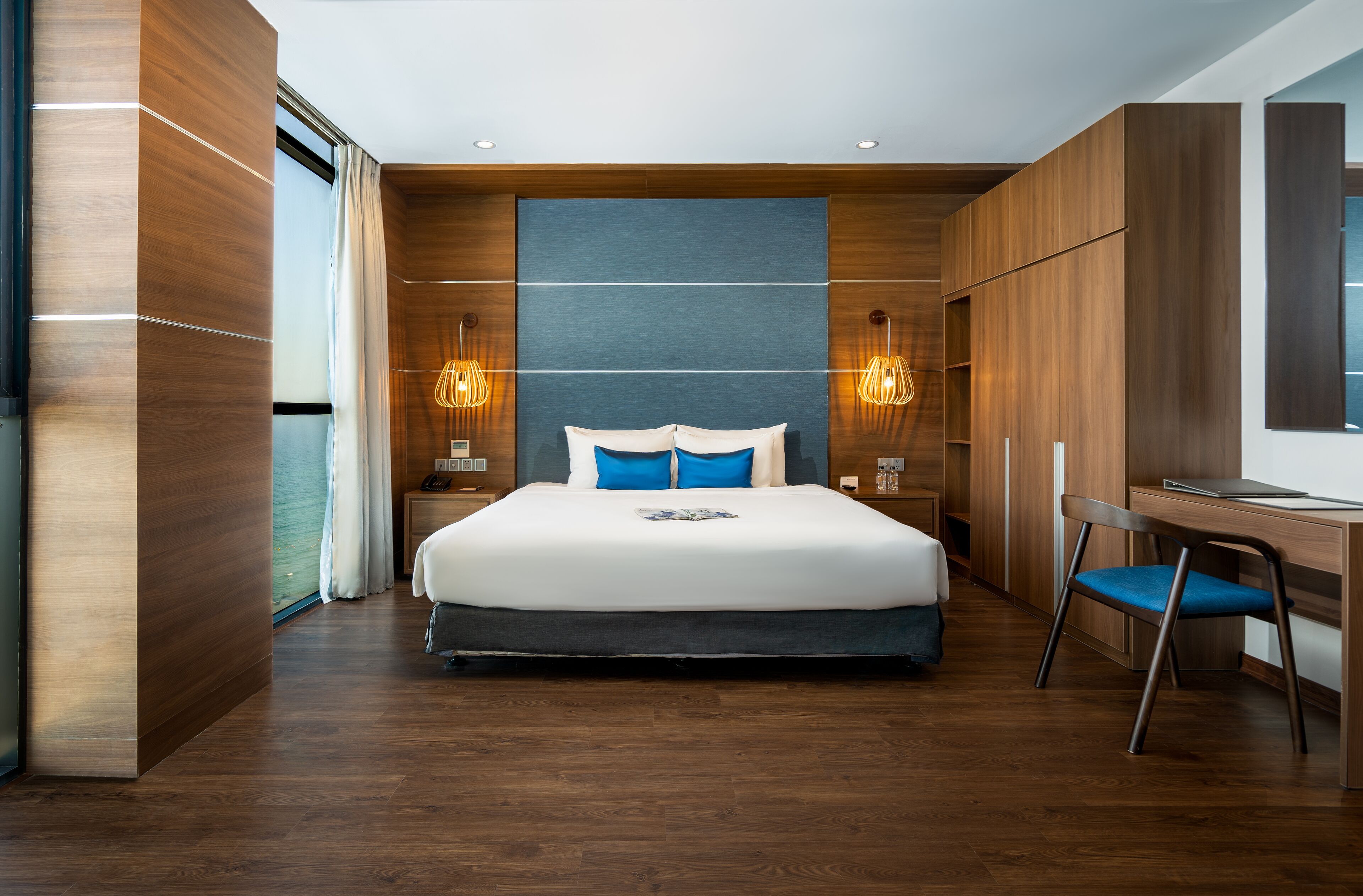 Een moderne hotelkamer met een groot bed, houten lambrisering en een bureau met stoel.