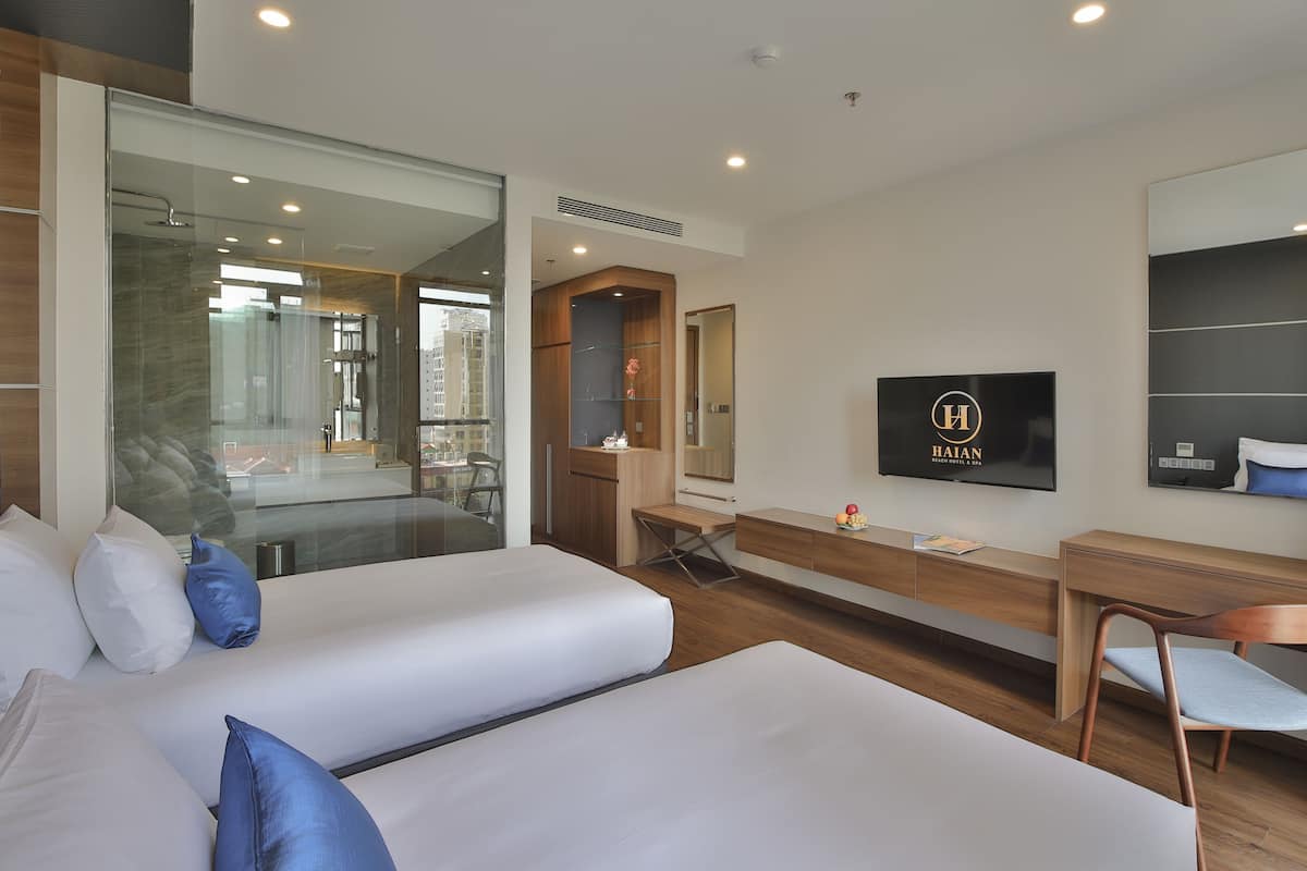 A modern hotel room with two beds, a desk, a TV, and a large mirror.