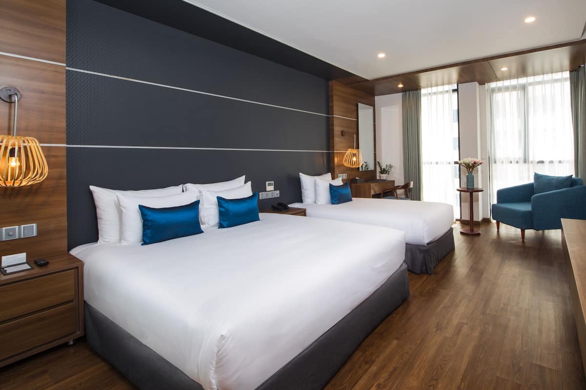 A modern hotel room with two beds, a desk, a chair, and a TV.