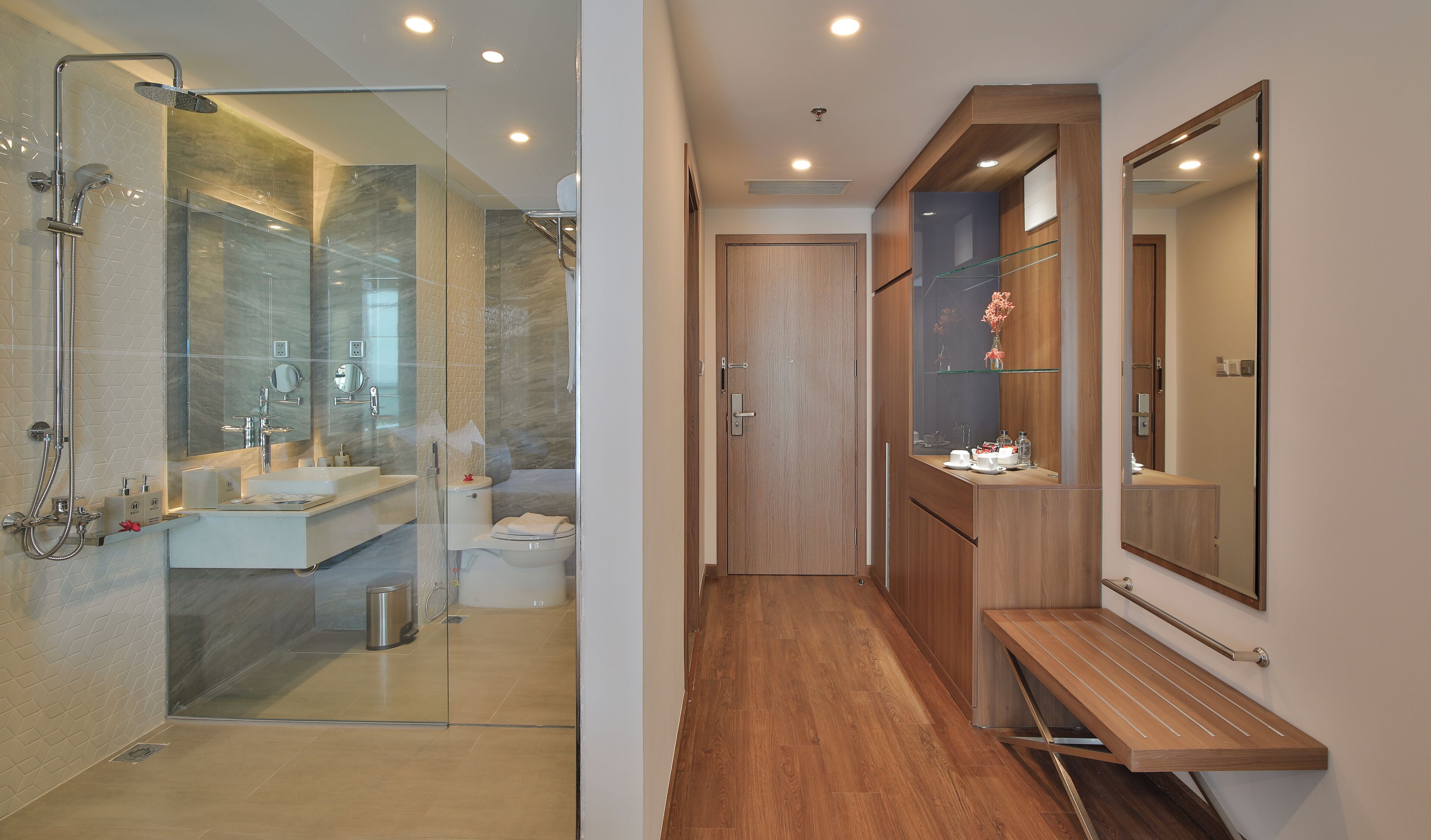 Un baño moderno con cabina de ducha de vidrio, tocador con espejo y banco de madera.