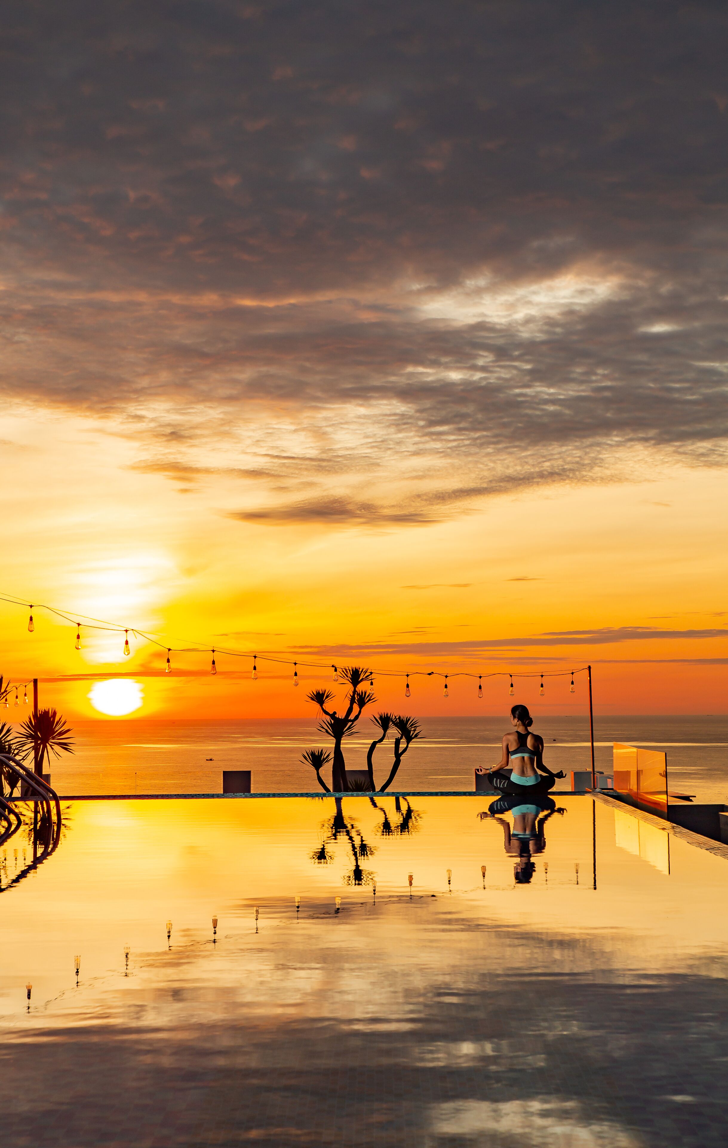 A sunset view from a rooftop pool area with string lights and palm trees.