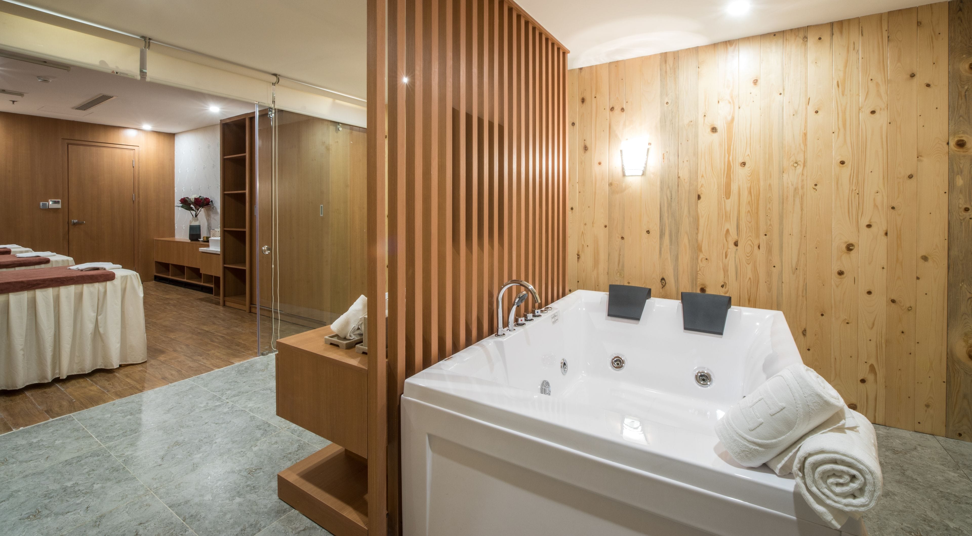 A modern bathroom with a large bathtub, wooden paneling, and a massage table area.