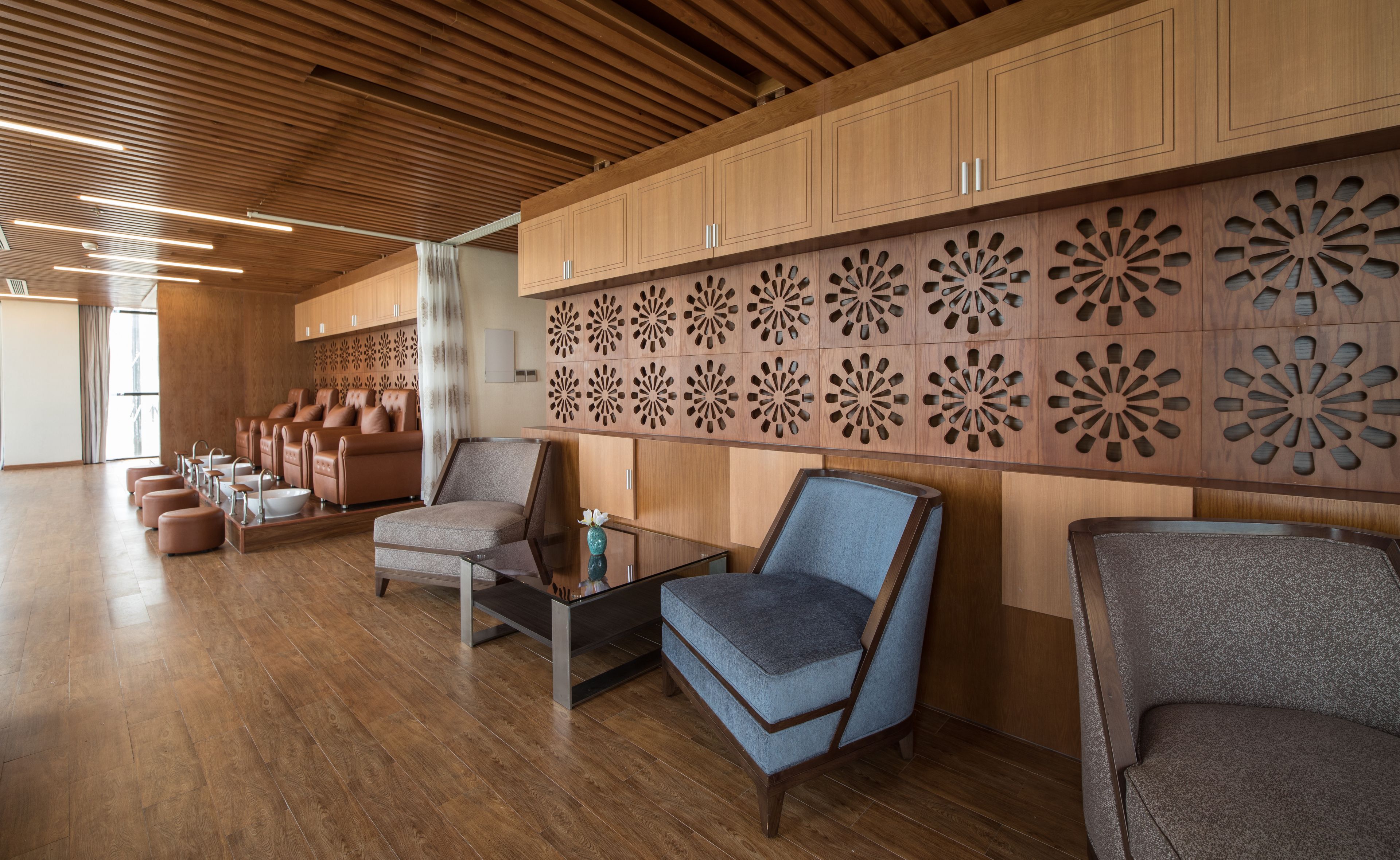 A spacious room with wooden flooring, a seating area with sofas and armchairs, and a decorative wall with geometric patterns.