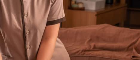 A massage therapy session in a room with a bed, a wooden cabinet, and a vase with flowers.