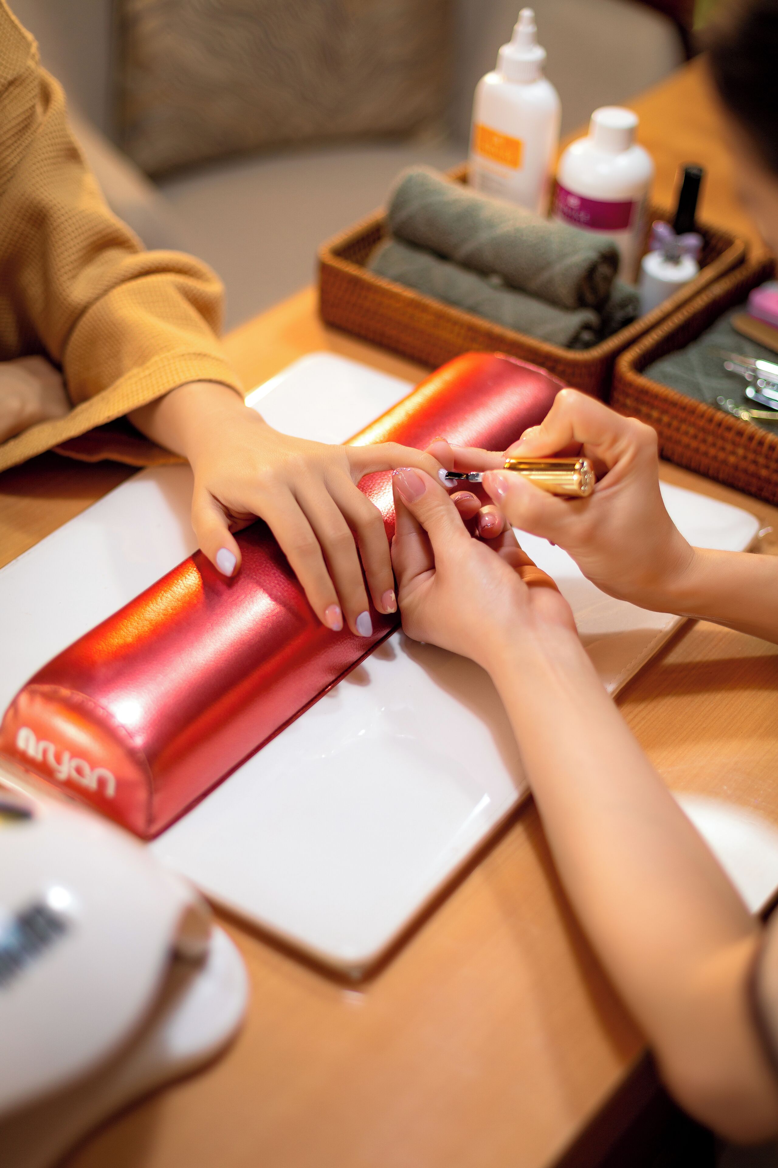 A close-up of hands getting a manicure, with nail polish and tools on a table.
