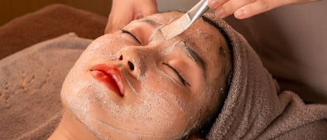 Una persona recostada en una cama, recibiendo un tratamiento facial con una toalla.