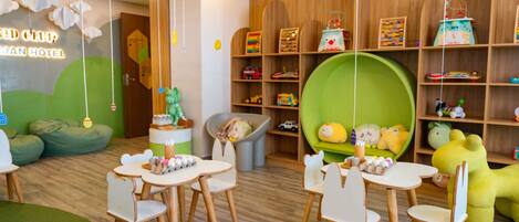 A children's playroom with green bean bag chairs, a green sofa, and a play area with toys and educational items.