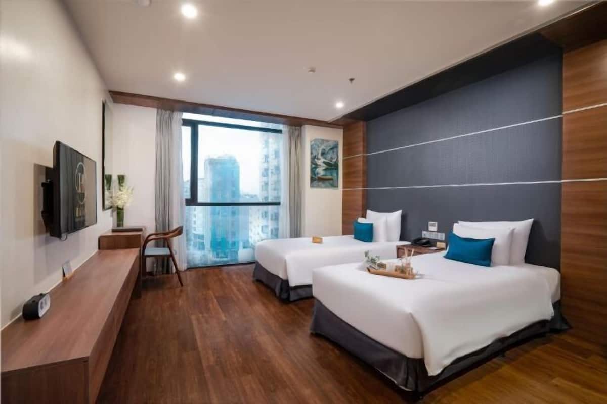 A hotel room with two beds, a desk, a TV, and a large window with a city view.