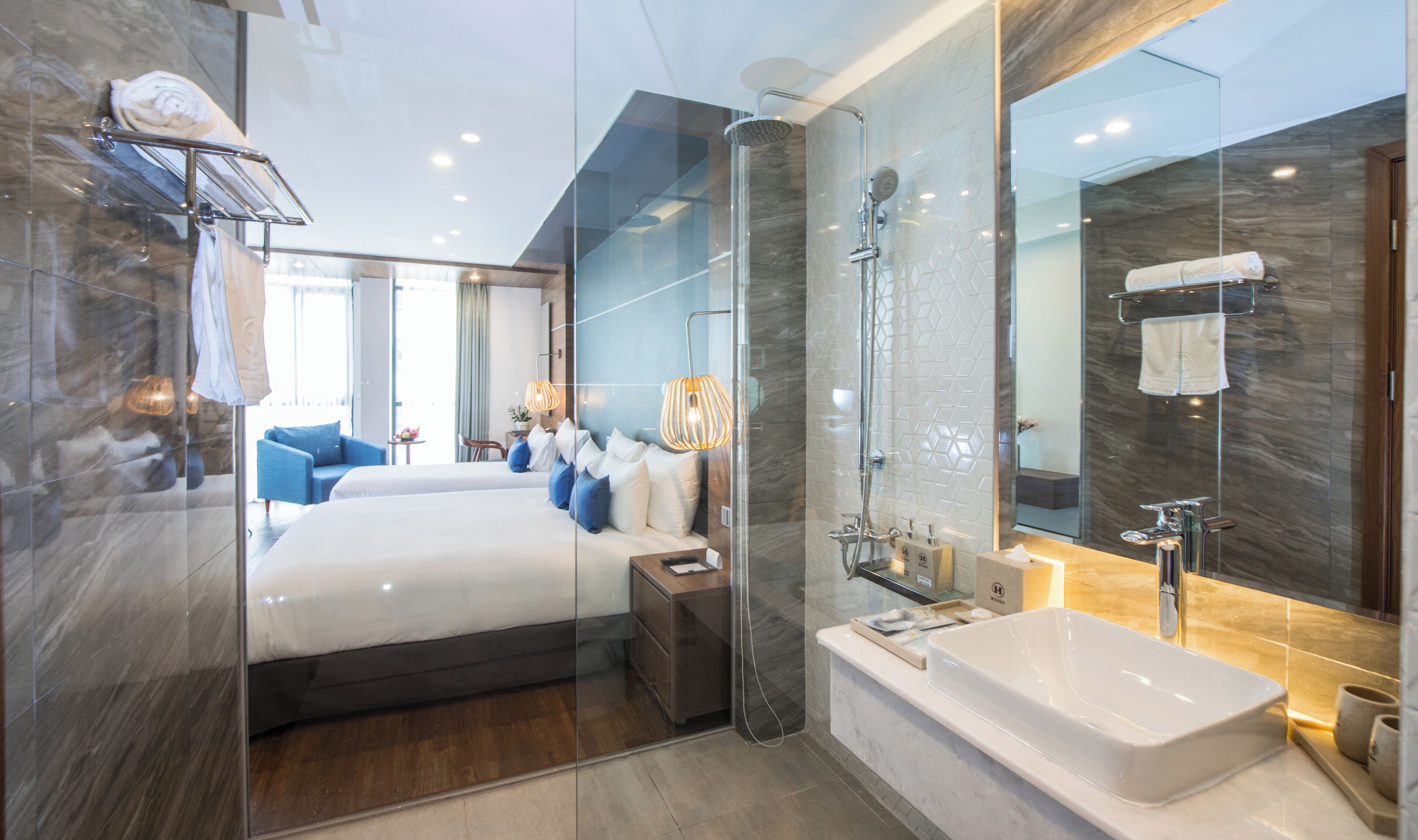 Una habitación de hotel moderna con una cama grande, ducha con paredes de vidrio, baño separado con bañera y un espejo amplio.