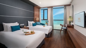 A hotel room with two beds, a desk, a chair, a TV, and a large window with a view of the ocean. - HAIAN Beach Hotel & Spa (Da Nang)