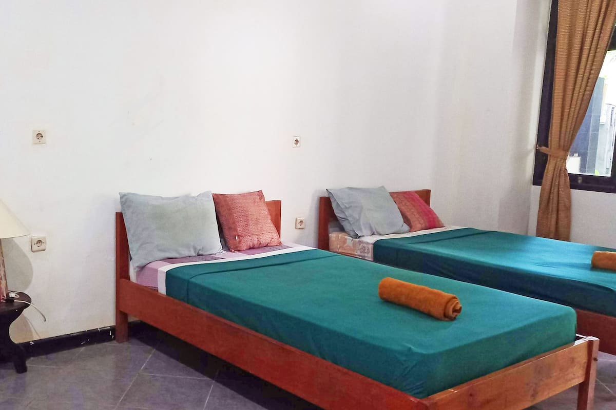 A room with two wooden beds, a small table, and a lamp.