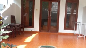 A spacious room with a wooden floor, a dining table with chairs, and a large window with a view of the outside. - Gili Welldone Guesthouse (Gili Trawangan)