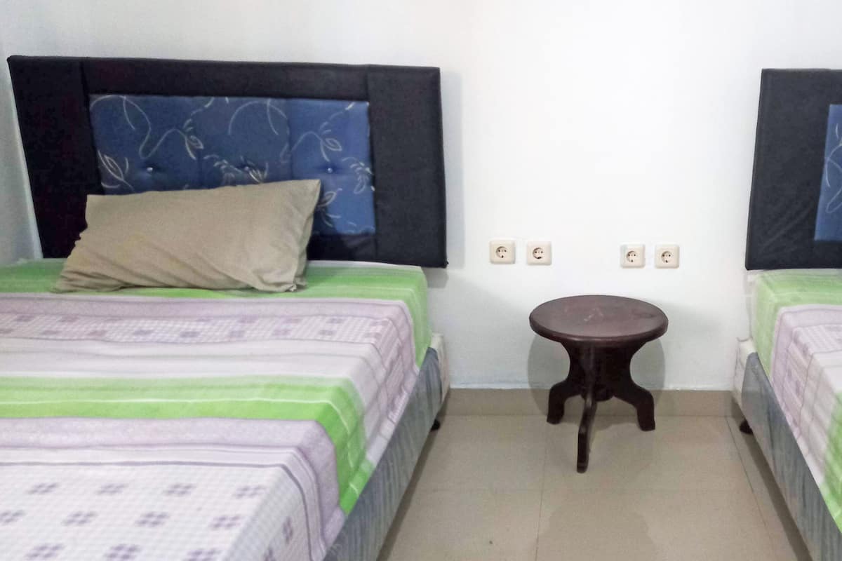 A room with two beds, each with a headboard, a small round table, and a plain white wall with three electrical outlets.
