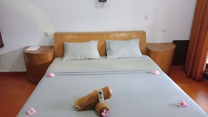 A neatly made bed with pillows, a wooden headboard, and a bedside table with a remote control. - Gili Welldone Guesthouse (Gili Trawangan)