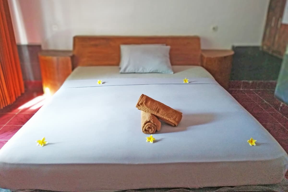 A neatly made bed with a rolled towel and decorative flowers, a wooden headboard, and a light-colored wall.