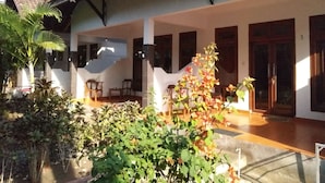 A covered outdoor area with a tiled floor, wooden furniture, and potted plants. - Gili Welldone Guesthouse (Gili Trawangan)