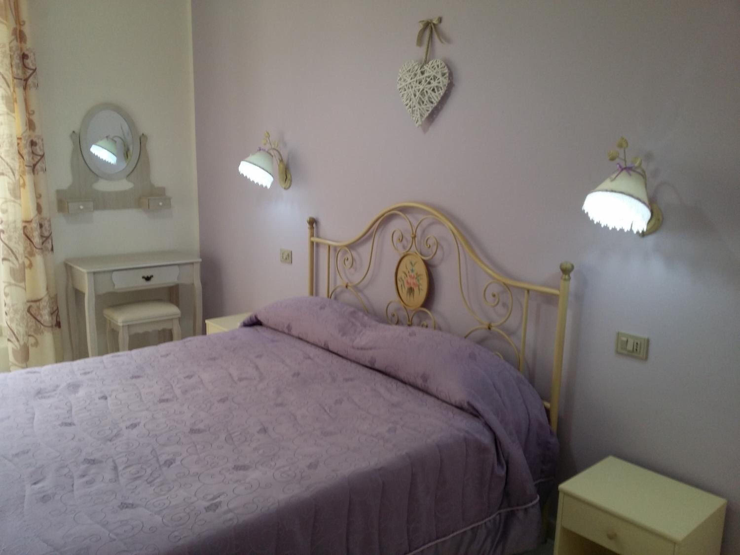 Quarto com cama, mesas de cabeceira, cômoda e luminárias na parede.