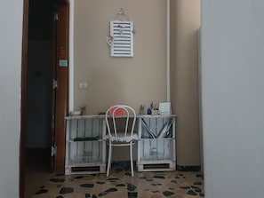 Une petite pièce avec une chaise blanche, une table sur laquelle se trouvent quelques objets et une étagère fixée au mur, ornée d’un décor en forme de cœur.