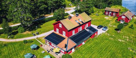 Een rode woning met een dak van zonnepanelen, omringd door een verzorgd gazon en een klein vijvertje.