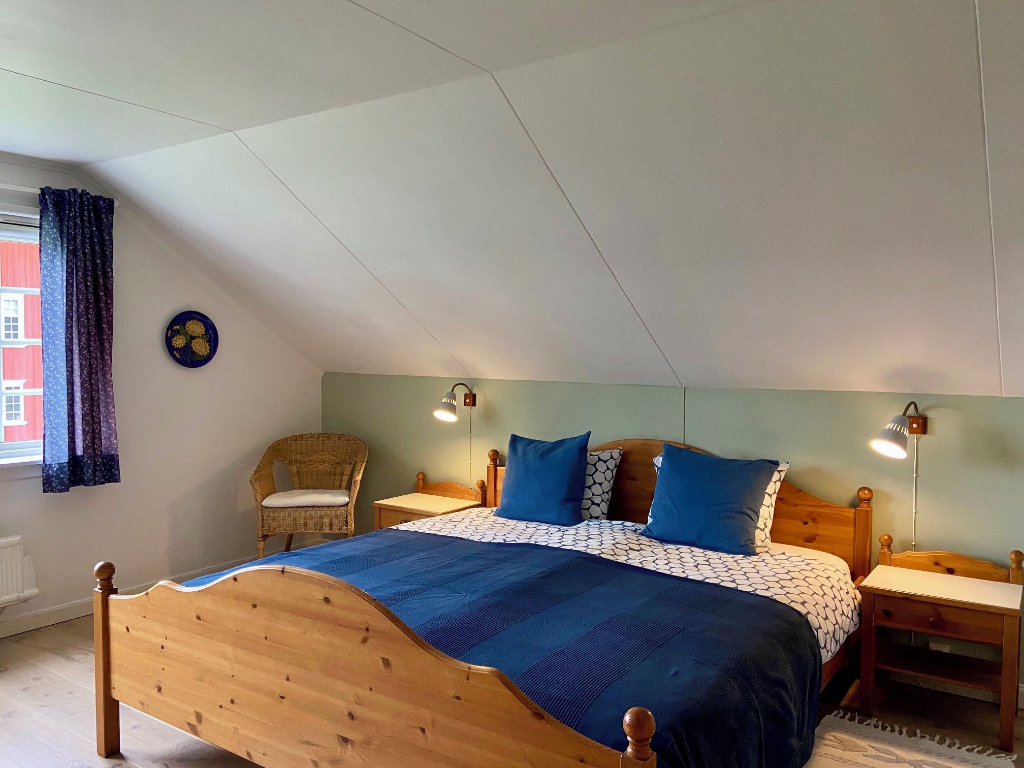 A bedroom with a wooden bed, two bedside tables, a chair, and a wall-mounted lamp.