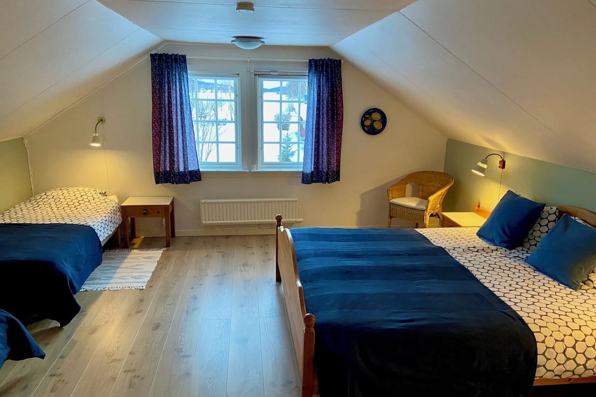Et værelse med to senge, et vindue med gardiner, en radiator, en stol og et vægur.