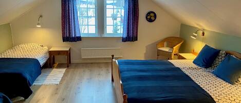 A room with two beds, a window with curtains, a radiator, a chair, and a wall clock.