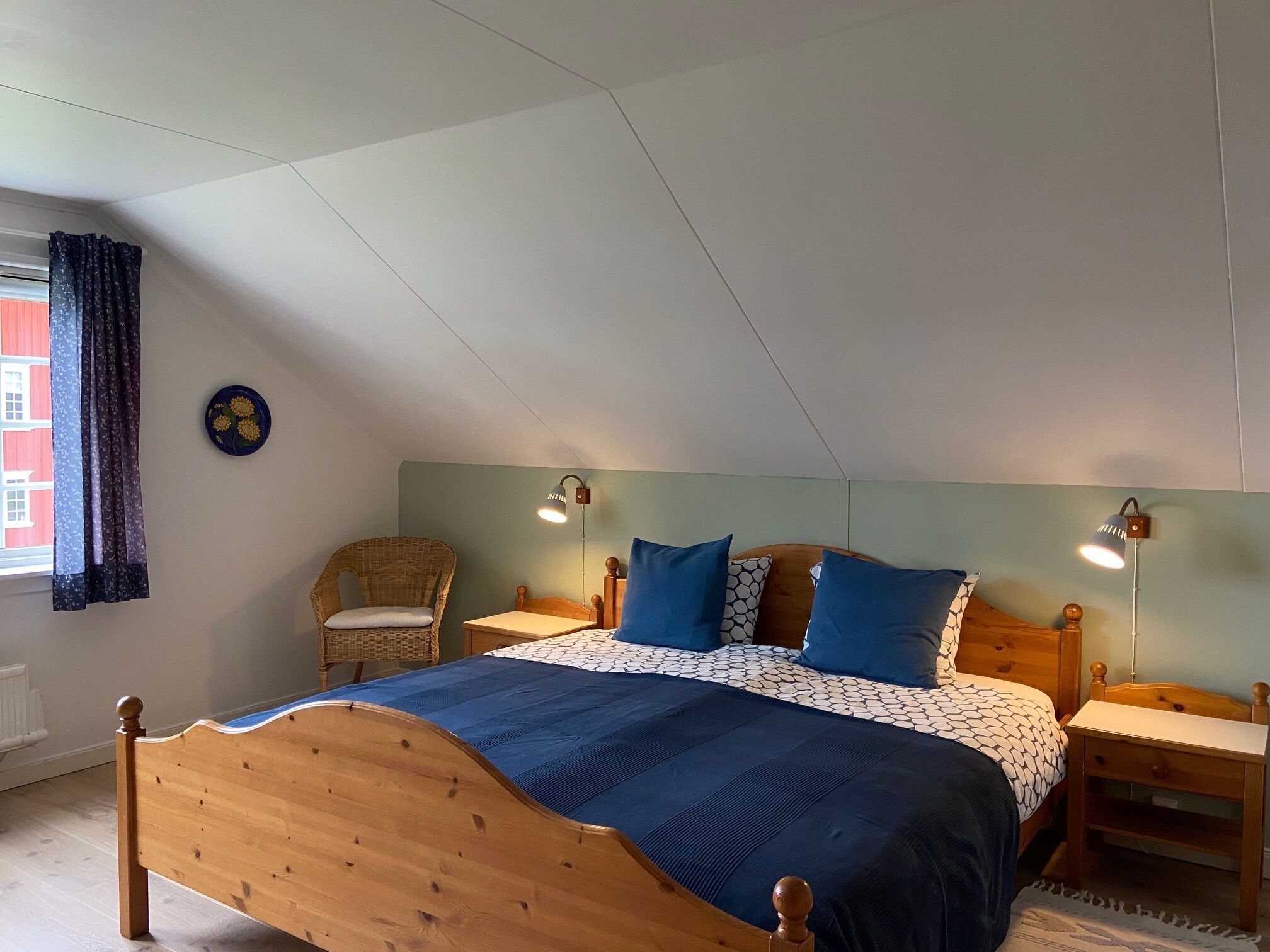 Un dormitorio con una cama de madera, dos mesitas de noche, una silla, una lámpara de pared y una ventana con cortinas.