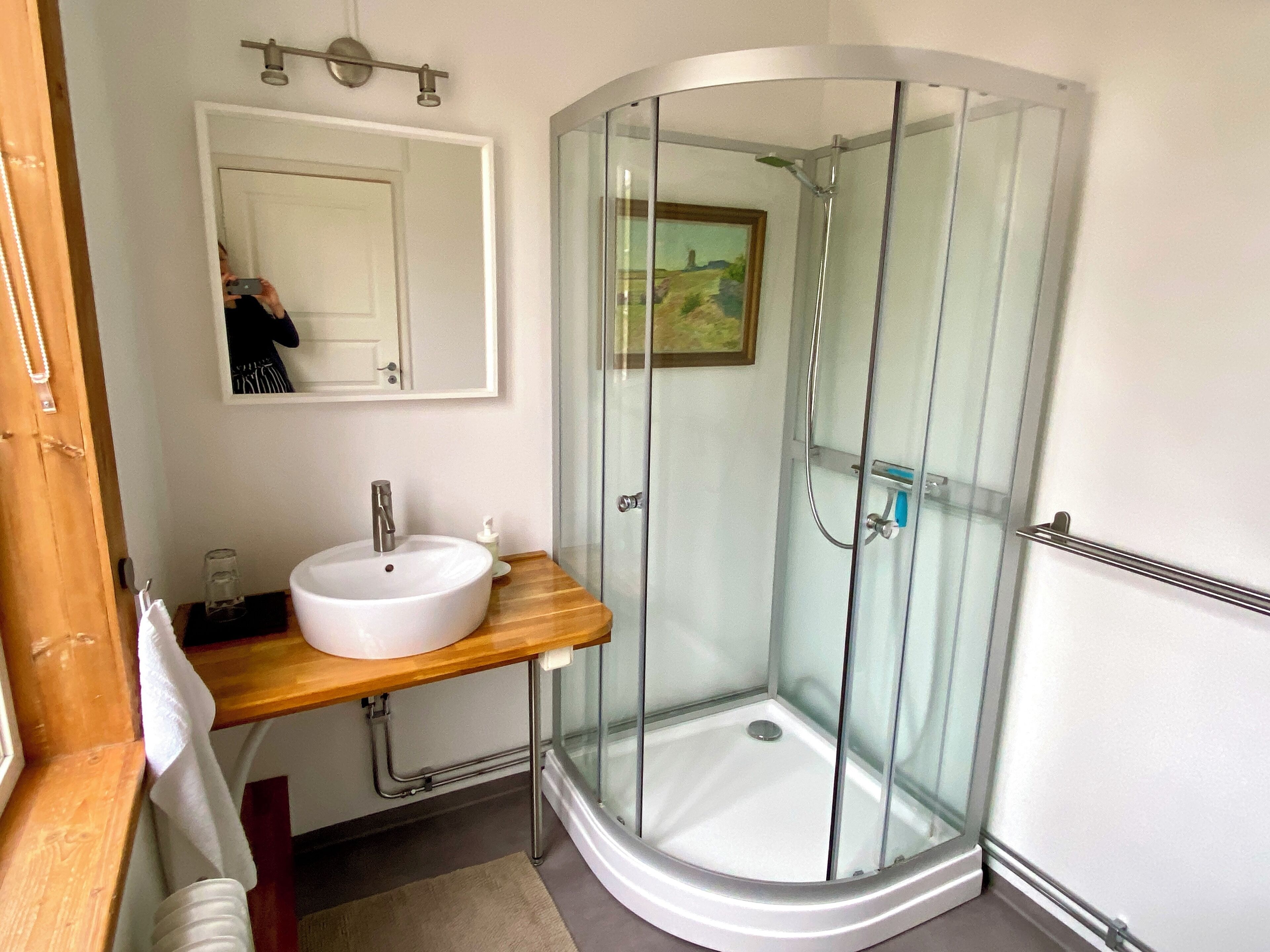 Een moderne badkamer met een douchecabine van glas, een witte wastafel en een houten aanrecht.