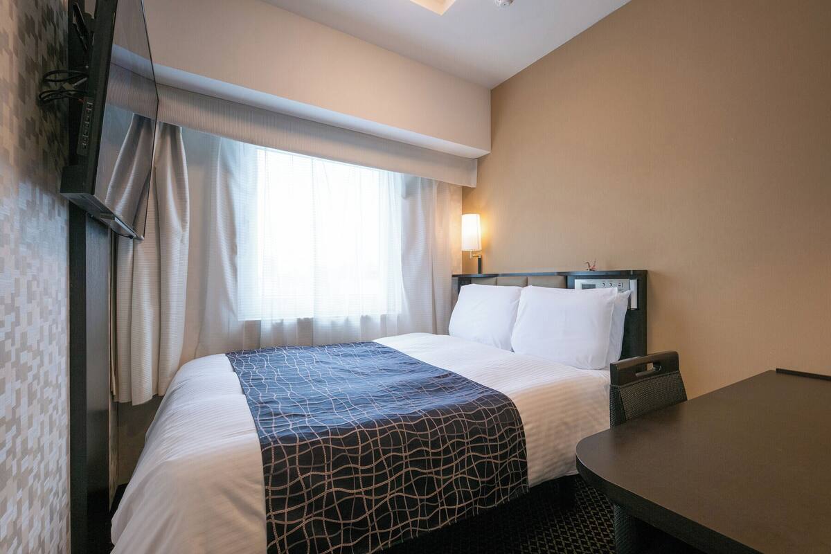Une chambre d’hôtel avec un lit, une table de chevet, une lampe et une fenêtre avec des rideaux.