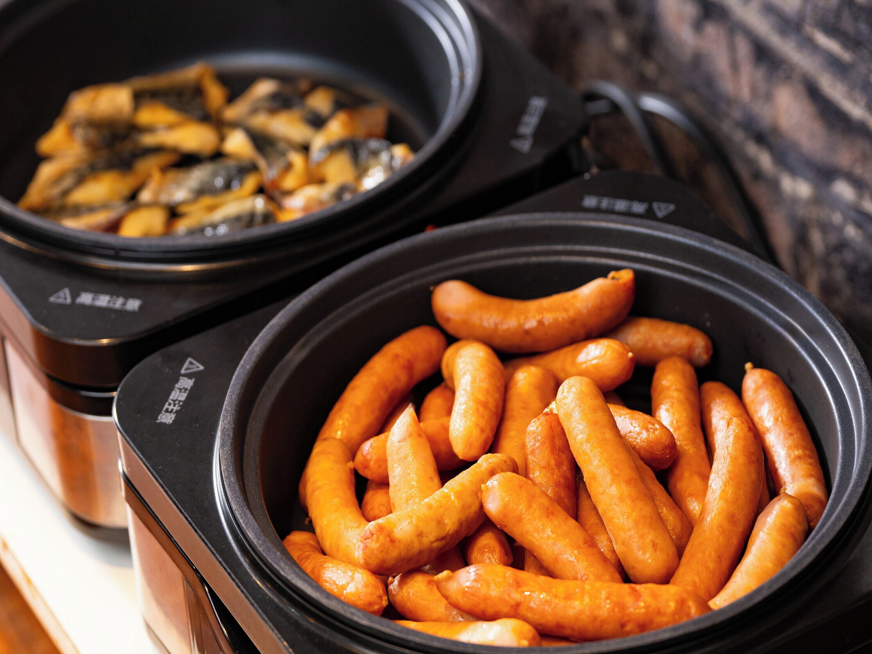 Two black slow cookers filled with sausages and mushrooms.