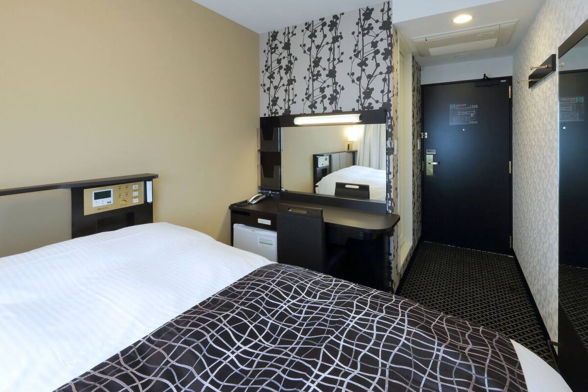 Une chambre d’hôtel avec un lit, un bureau avec un téléphone, un miroir et une porte.