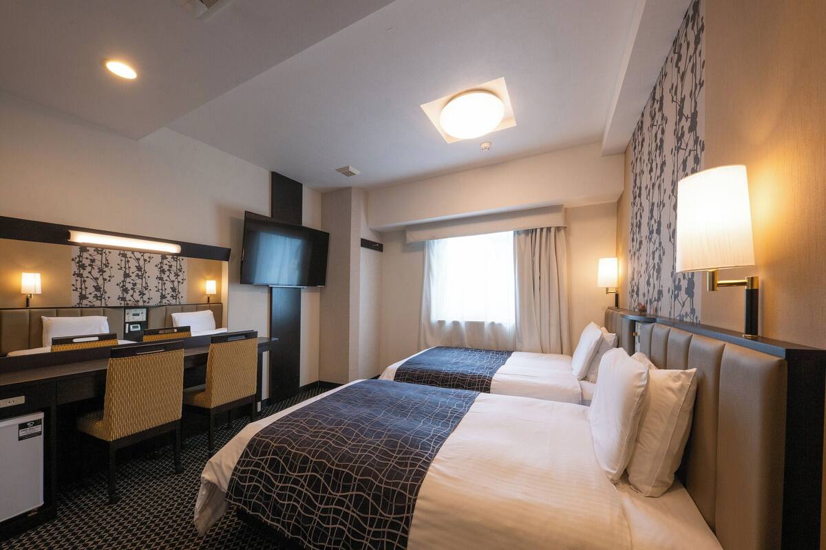 Une chambre d’hôtel avec deux lits, un bureau, une télévision et une fenêtre avec des rideaux.