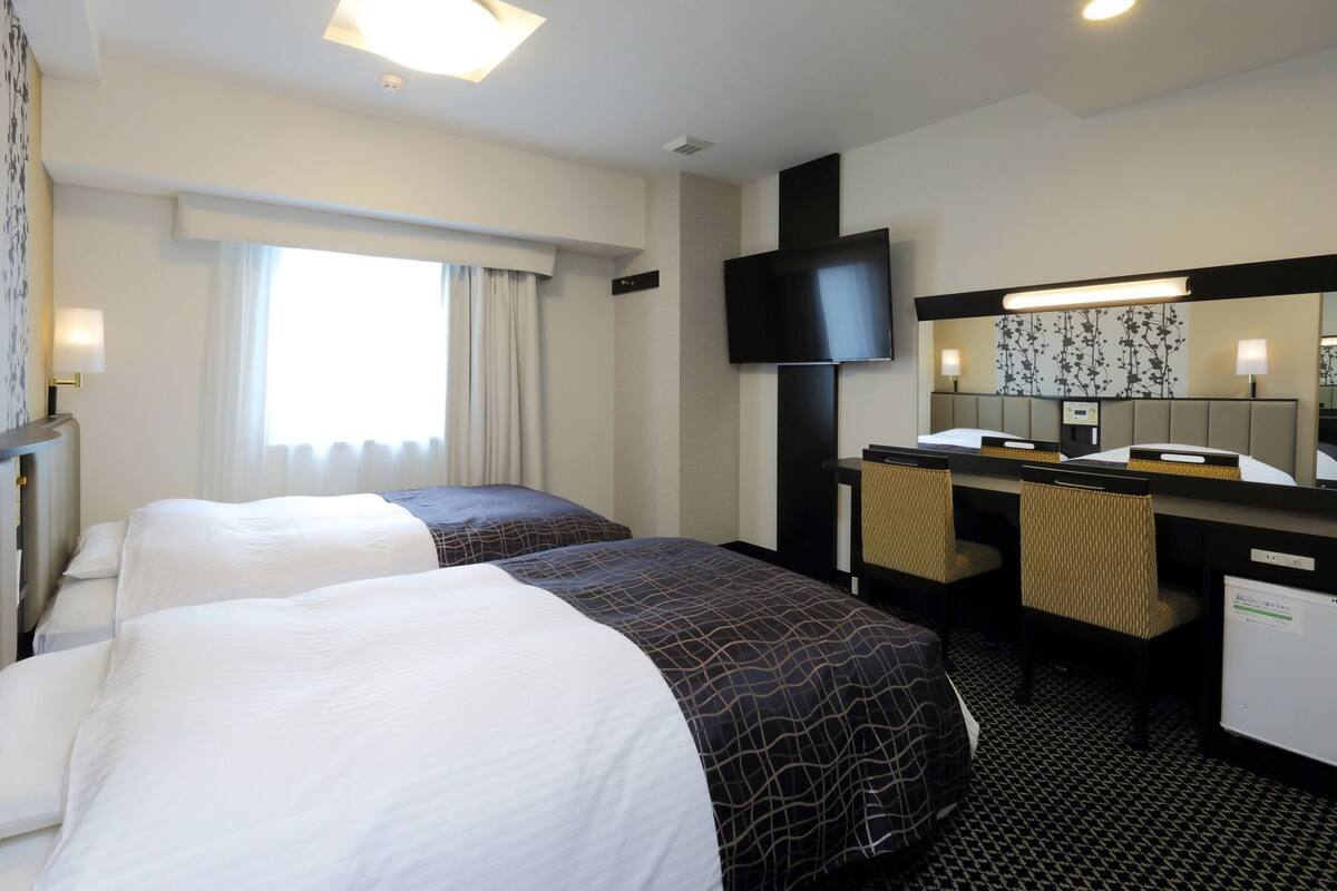 Une chambre d’hôtel avec deux lits, un bureau, une télévision et une grande fenêtre.