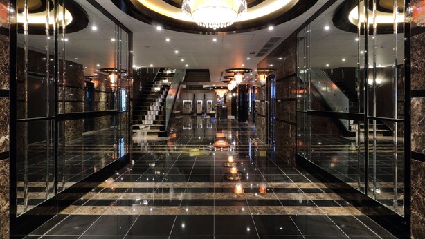 A modern lobby with a central staircase, glass walls, and a chandelier.