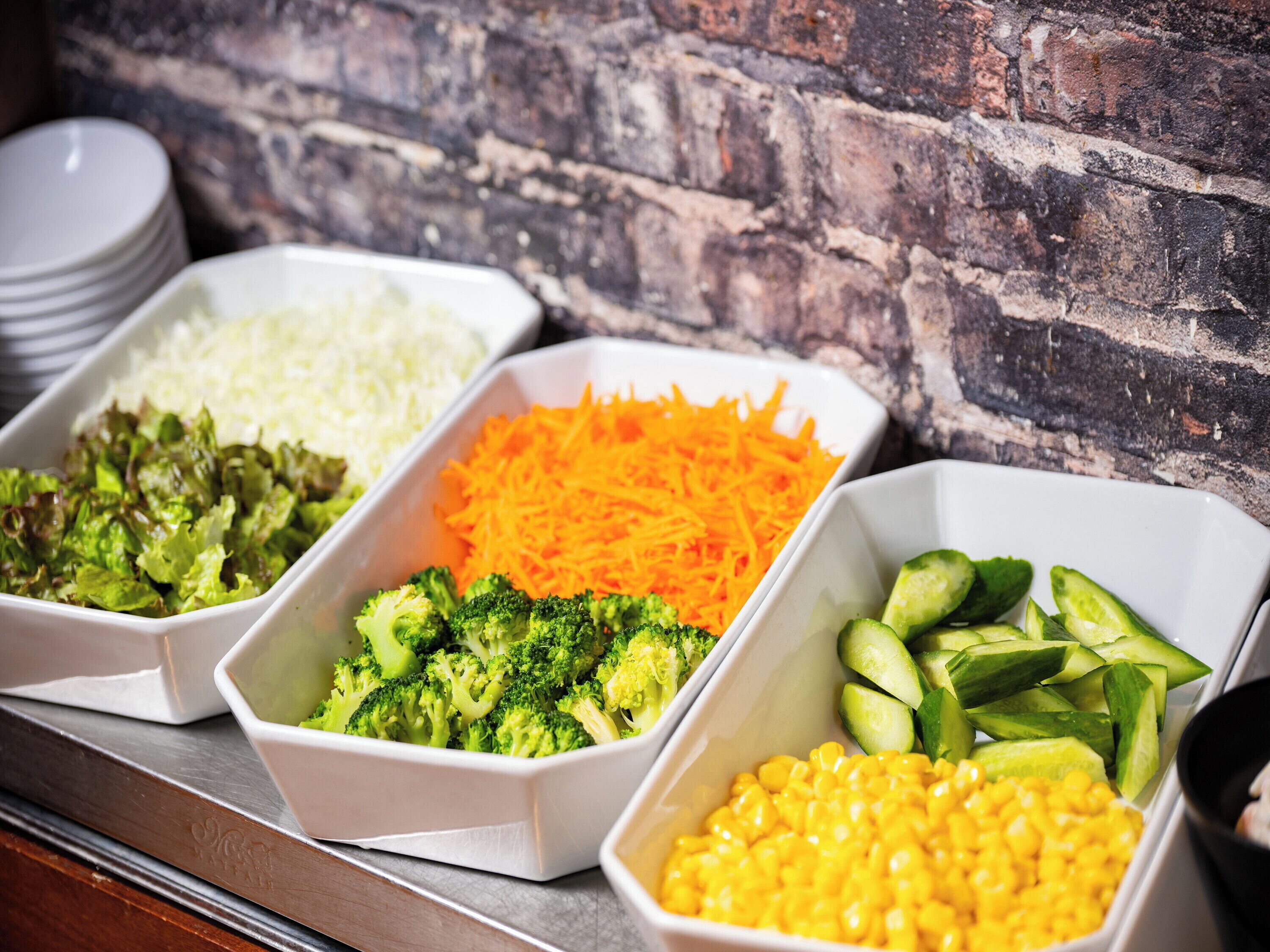 A buffet with various food items including broccoli, shredded carrots, and corn.
