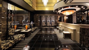 A modern hotel lobby with a black and gold color scheme, a chandelier, a reception desk, and a seating area with patterned sofas.