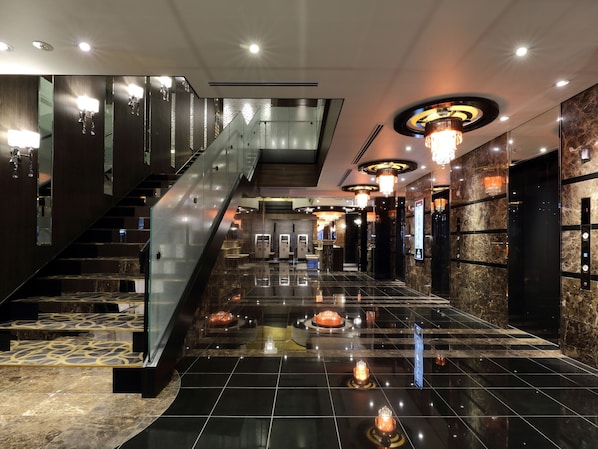 A modern hotel lobby with a central staircase, marble flooring, and contemporary lighting fixtures.