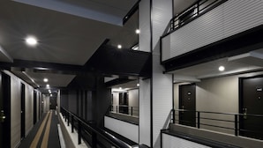 A modern hotel corridor with a central walkway, black railings, and multiple doors on both sides.