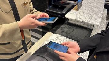 En person i en beige uniform betjener en smartphone ved en disk med en marmorbordplade.