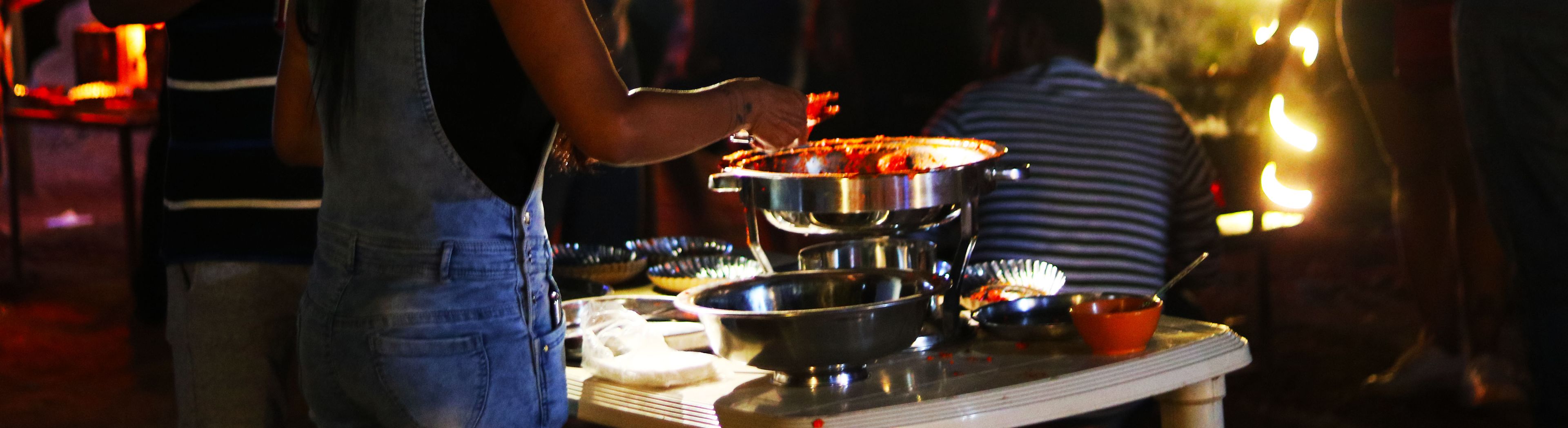 Una persona cocina en una estufa, con diferentes utensilios y alimentos sobre una mesa.