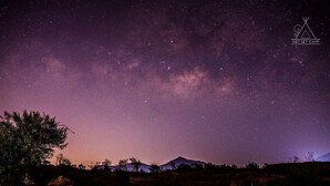 Cielo nocturno con estrellas y una montaña al fondo.