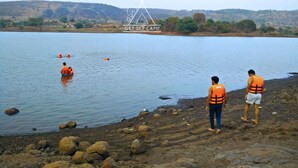 Un lago con gente usando chalecos salvavidas naranja, algunos en el agua y otros en la orilla.