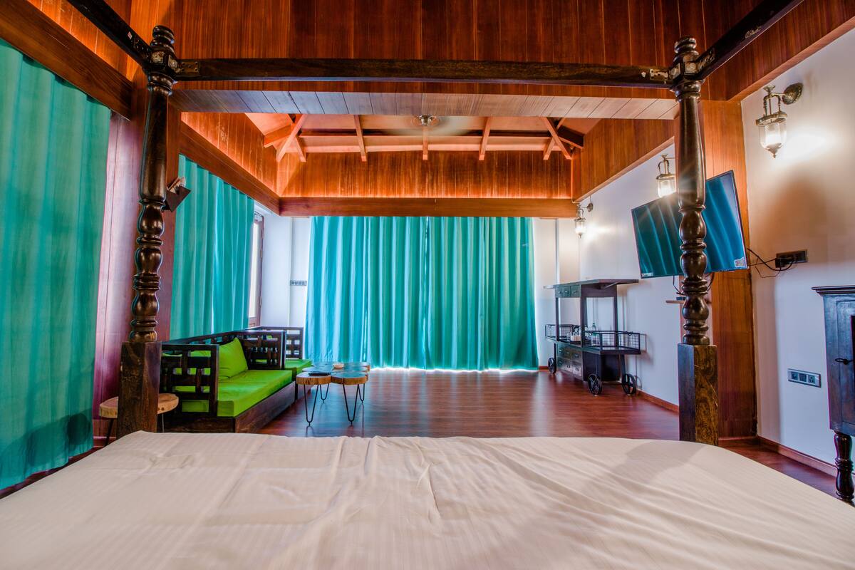 A spacious room with a large bed, a green sofa, and a wooden ceiling.