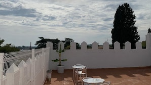 A rooftop terrace with a white fence, potted plants, and metal chairs. - El Castillo (Alcala de Guadaira)
