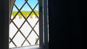 A window with a diamond-patterned grille, a clear view of a green field, and a white wall. - El Castillo (Alcala de Guadaira)