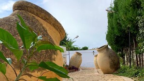A paved pathway leading to large stone structures, surrounded by greenery and potted plants. - El Castillo (Alcala de Guadaira)